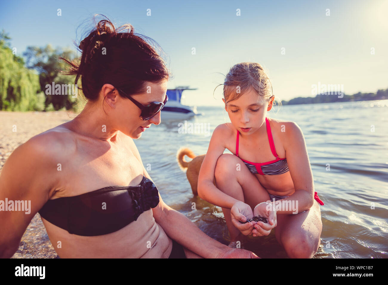 Mother, daughter and small yellow dog enjoying on the beach Stock Photo