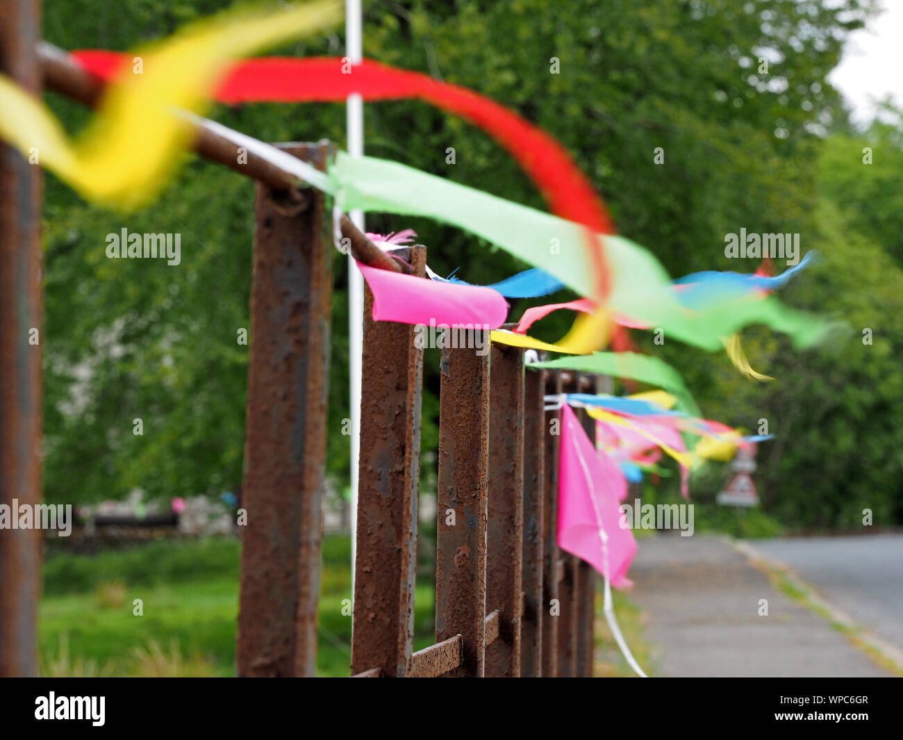 multi-coloured traditional bunting pennants fastened to rusty roadside railings flapping in the breeze in a village in Cumbria,England,UK Stock Photo