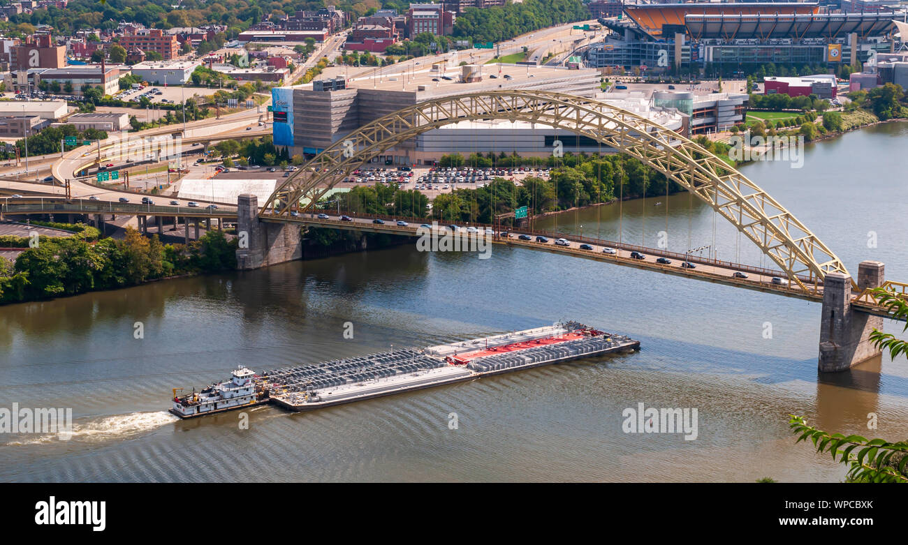 A loaded river barge under the West End bridge on the Ohio river with the  Rivers Casino and Heinz Field in the background in summer time, Pgh, PA, USA  Stock Photo 