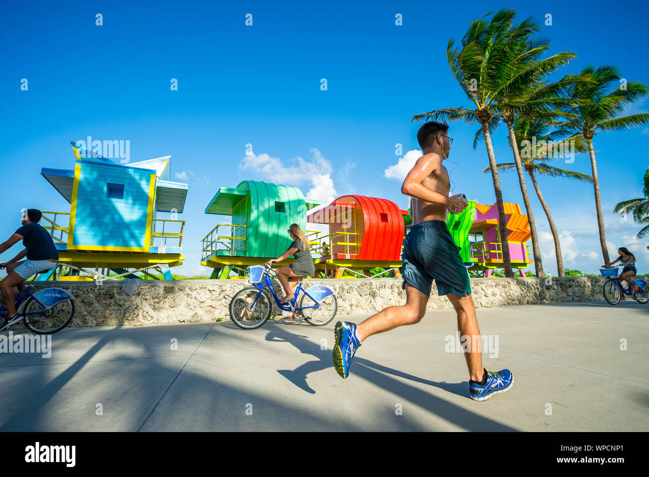 MIAMI - JULY 15, 2017: People pass along the Miami Beach promenade in front of vibrantly colored newly constructed lifeguard towers awaiting placement Stock Photo