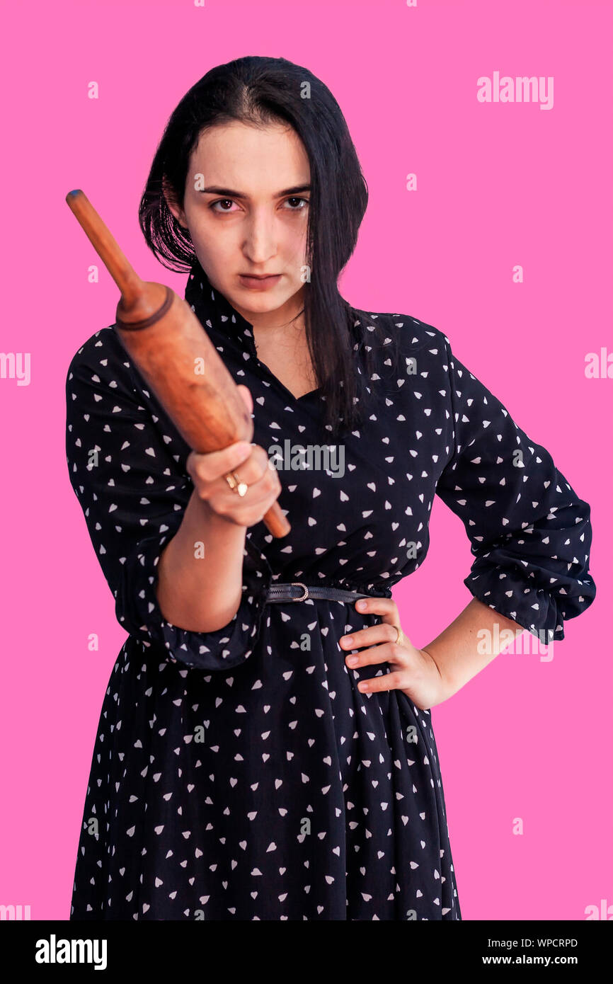 Angry wife waiting for her husband. Aggressive young middle-eastern woman holding dough rolling pin Stock Photo
