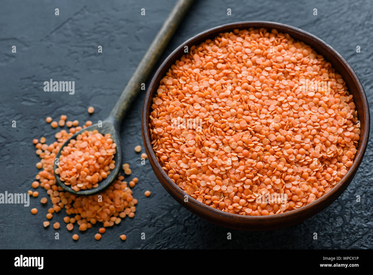 Dry red lentils in bowl on black background. Healthy vegan vegetarian