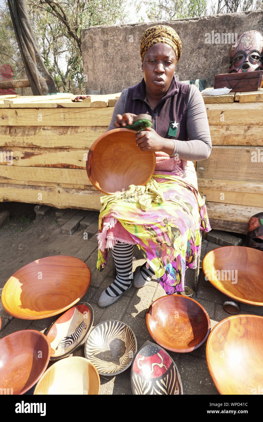 African woman street vendor sitting working on her wooden bowls that she sells at a market stall in Mpumalanga, South Africa works as informal trader Stock Photo