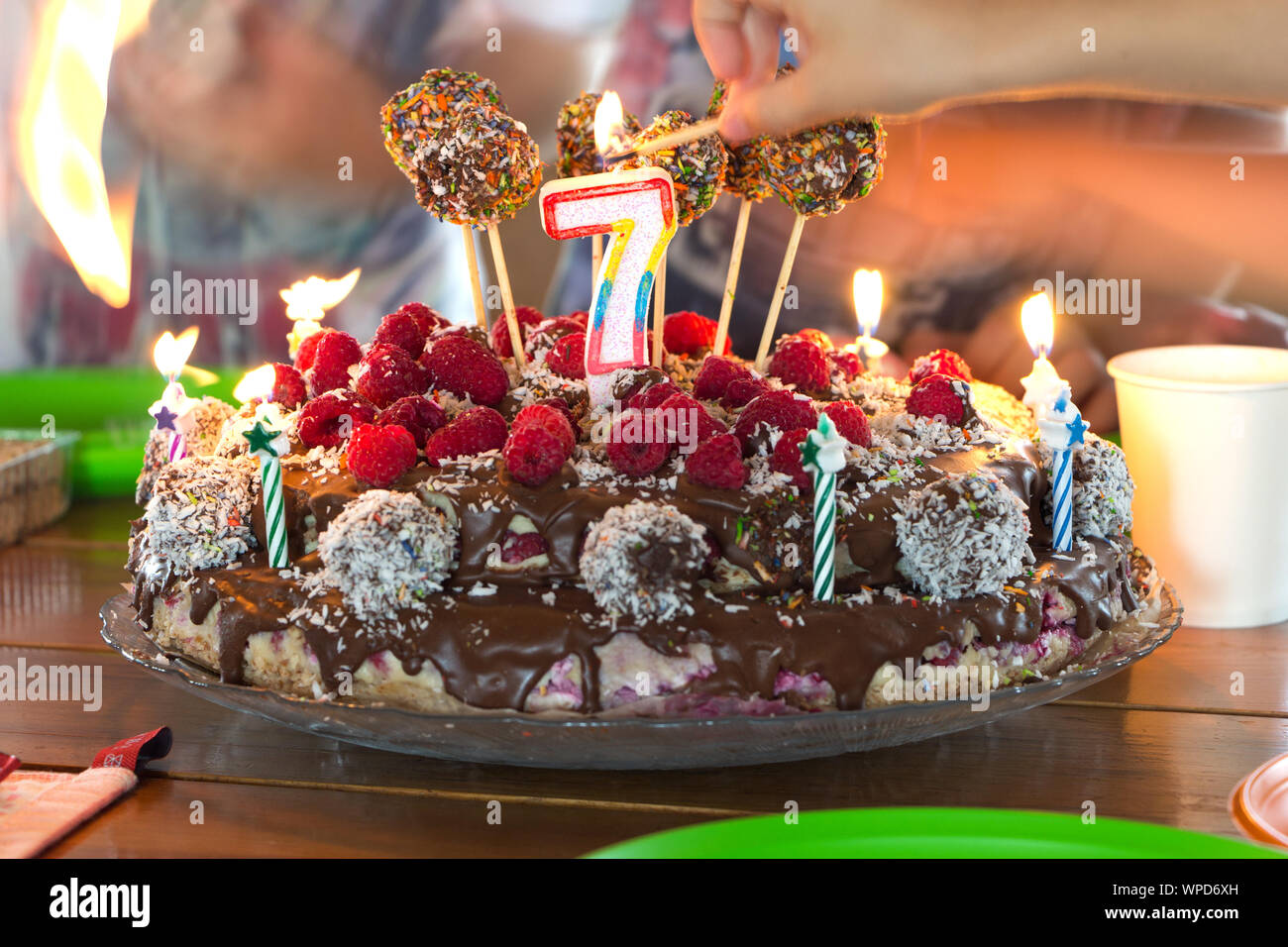 Setting fire to a candles on a childrens birthday cake. Selective focus on holiday candle in form of number 7, hands with burning matches in bokeh. Un Stock Photo