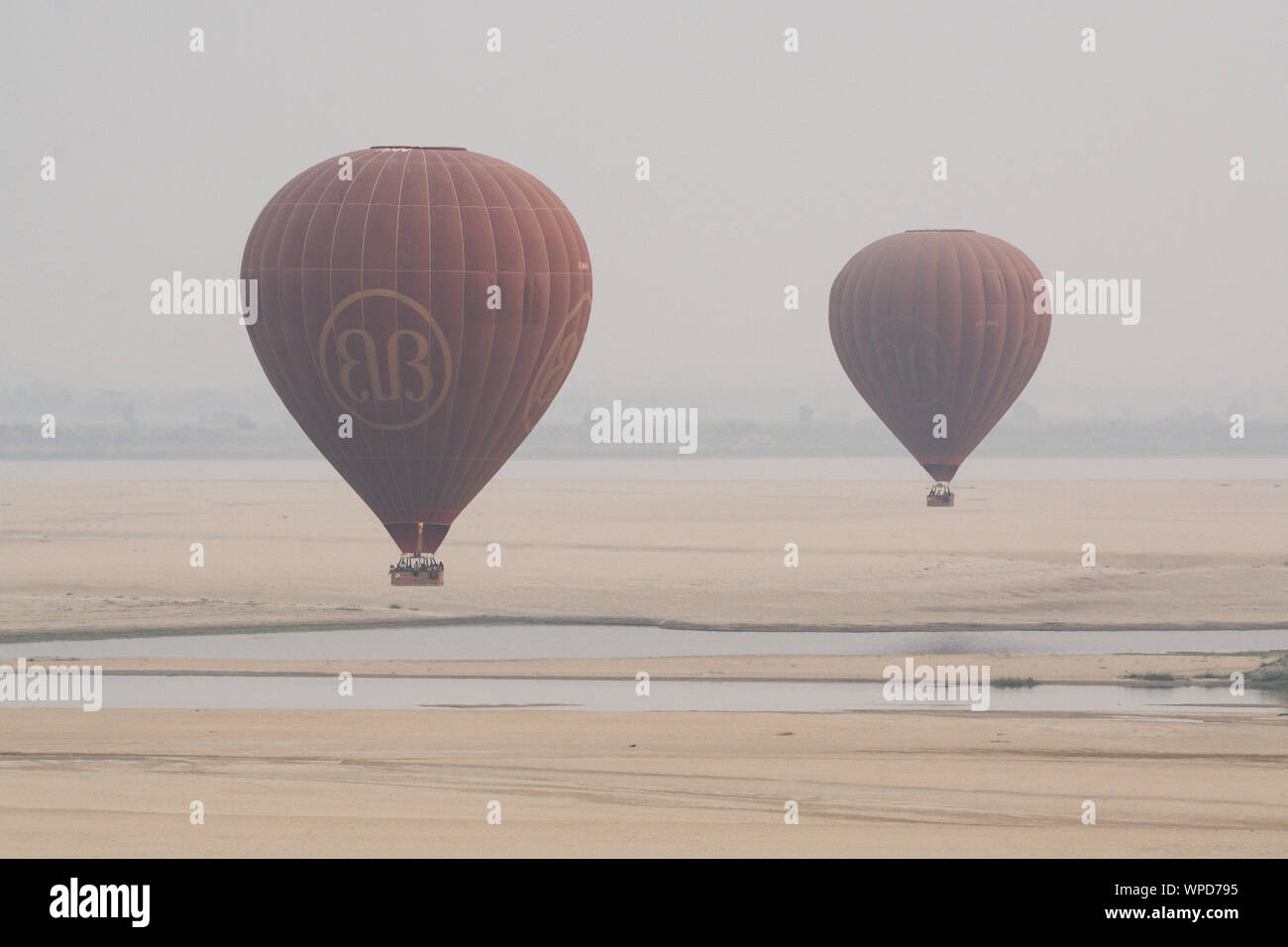 Bagan, Myanmar - March 2019: hot air balloons landing near Irrawaddy river at sunrise Stock Photo