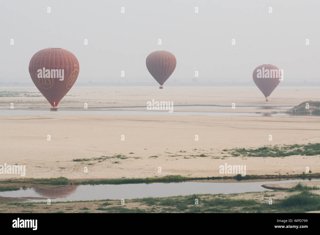 Bagan, Myanmar - March 2019: hot air balloons landing near Irrawaddy river at sunrise Stock Photo