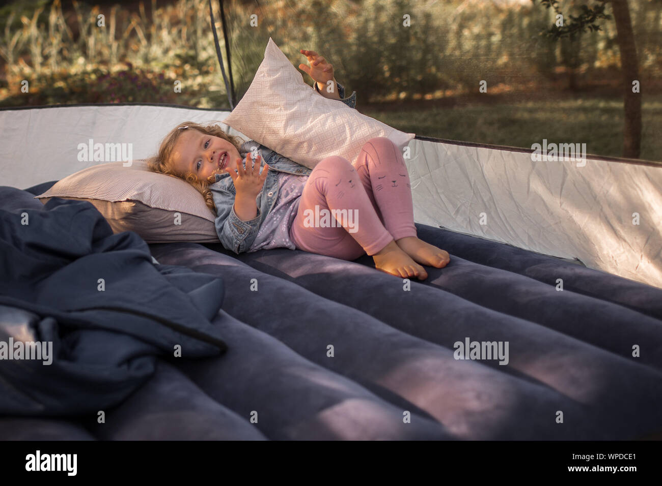 Little, happy preschooler girl, lying on air mattress in tent, on a camping trip Stock Photo