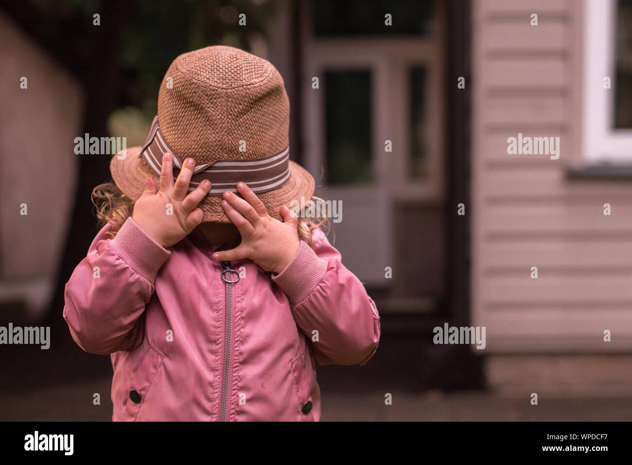 Child hiding her face under big adult summer straw hat Stock Photo