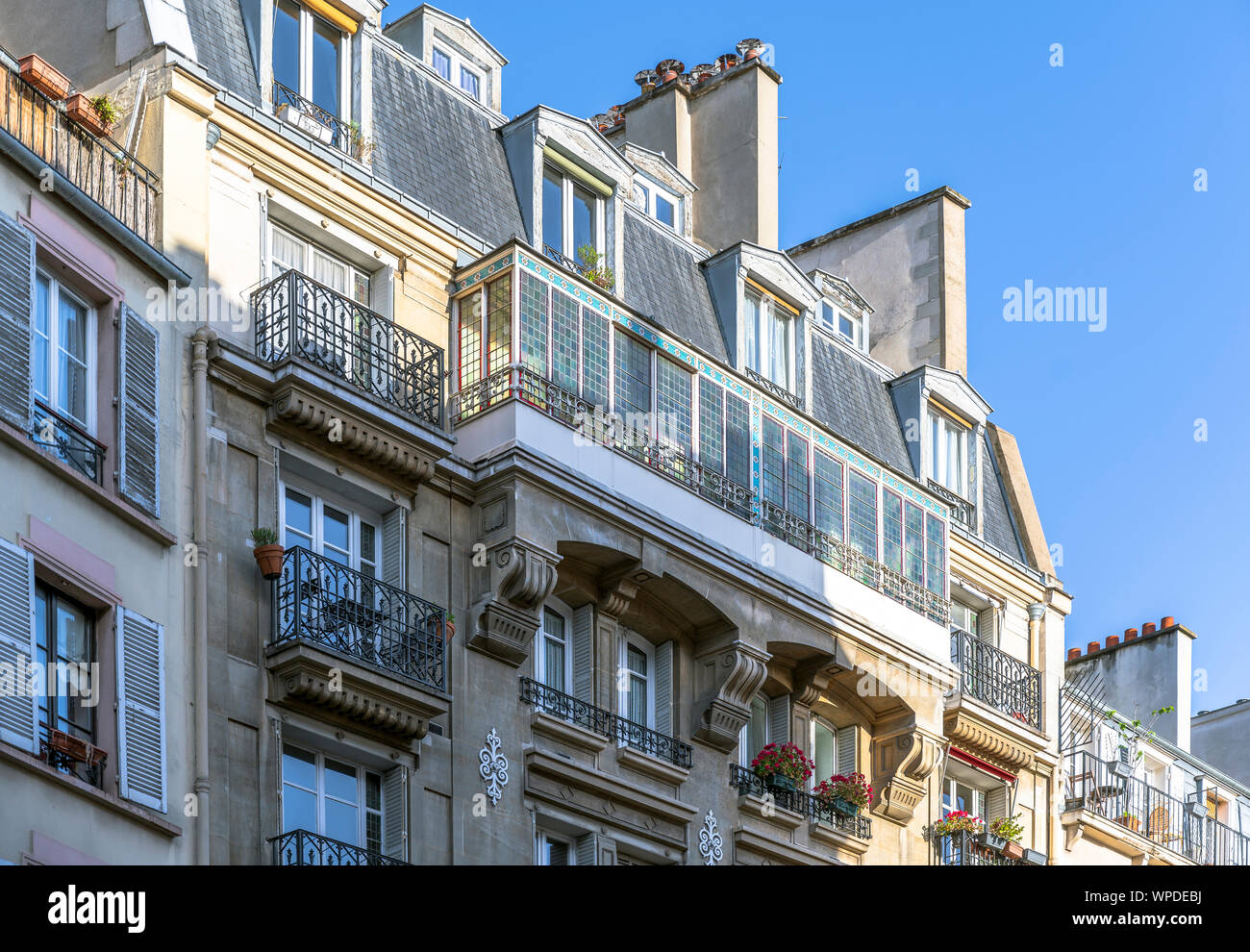 Hanging flower pots in the windows of the attic floor and on the balcony of multistory apartment building - a classic architectural design of old Pari Stock Photo