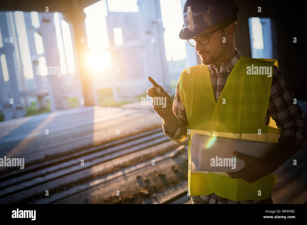 Male architect with blueprints using walkie-talkie Stock Photo