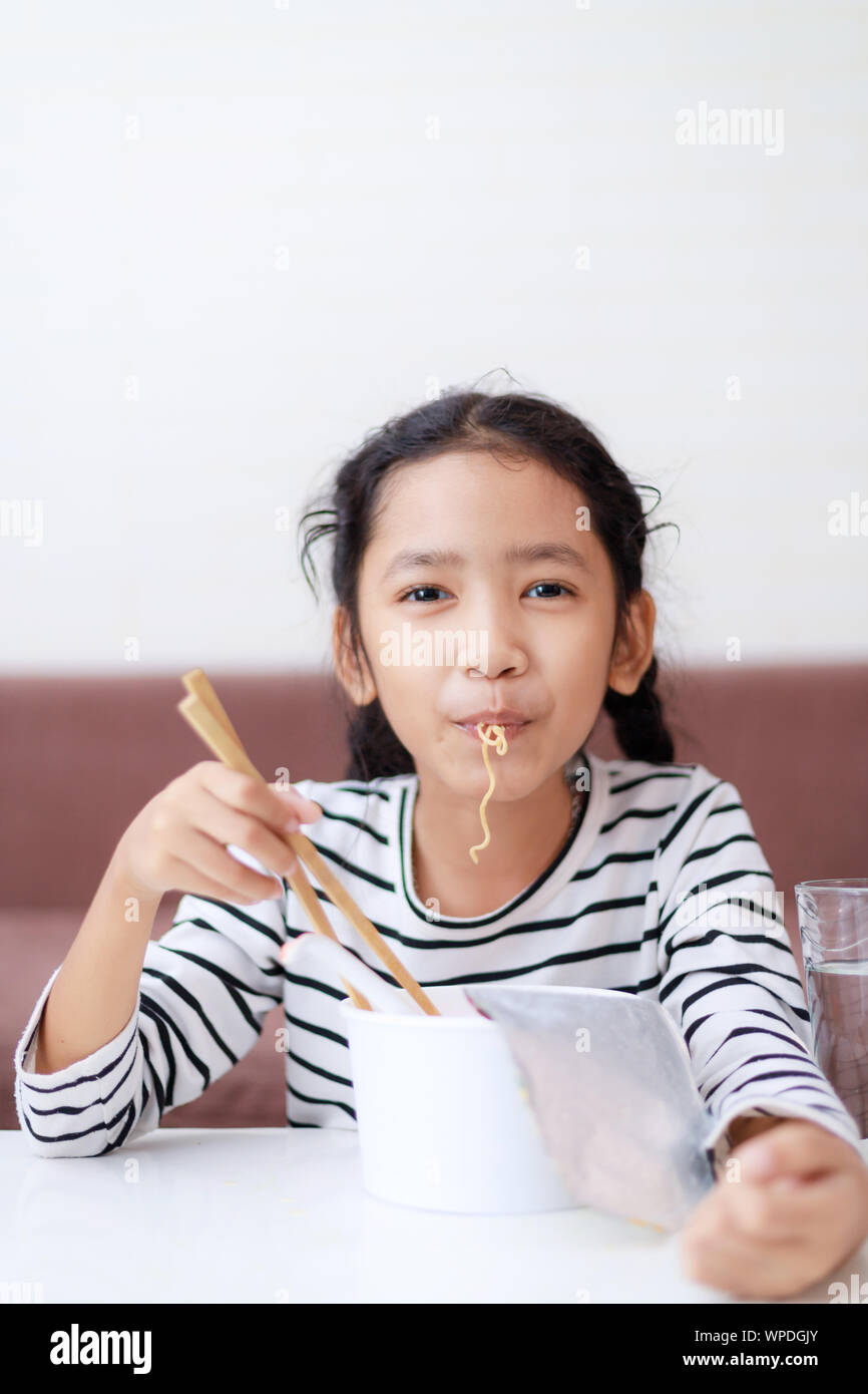 Happy little Asian girl sitting at white table to eating instant noodle  with deliciously select focus shallow depth of filed Stock Photo