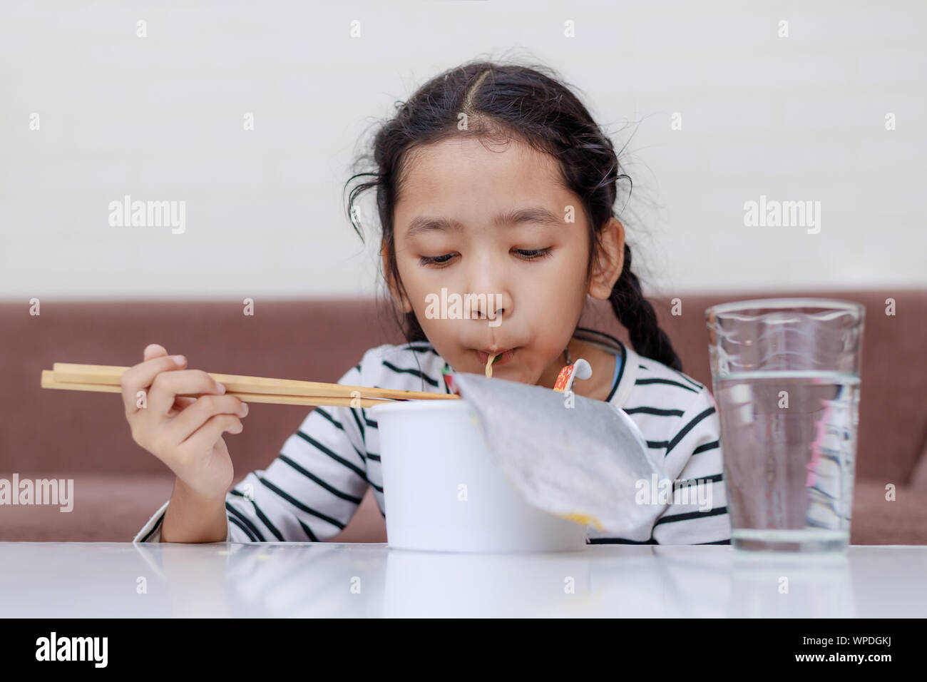 Little Asian girl sitting at white table to eating instant noodle and smile select focus shallow depth of filed Stock Photo