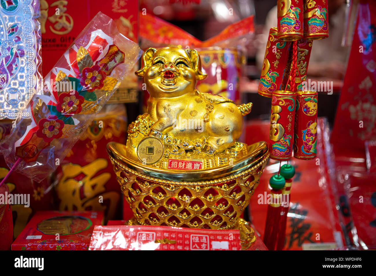 Plastic, golden figurine of Pig for this years Chinese Year of the Pig. On shelve surrounded by traditional red and golden decoration items in shop. Stock Photo