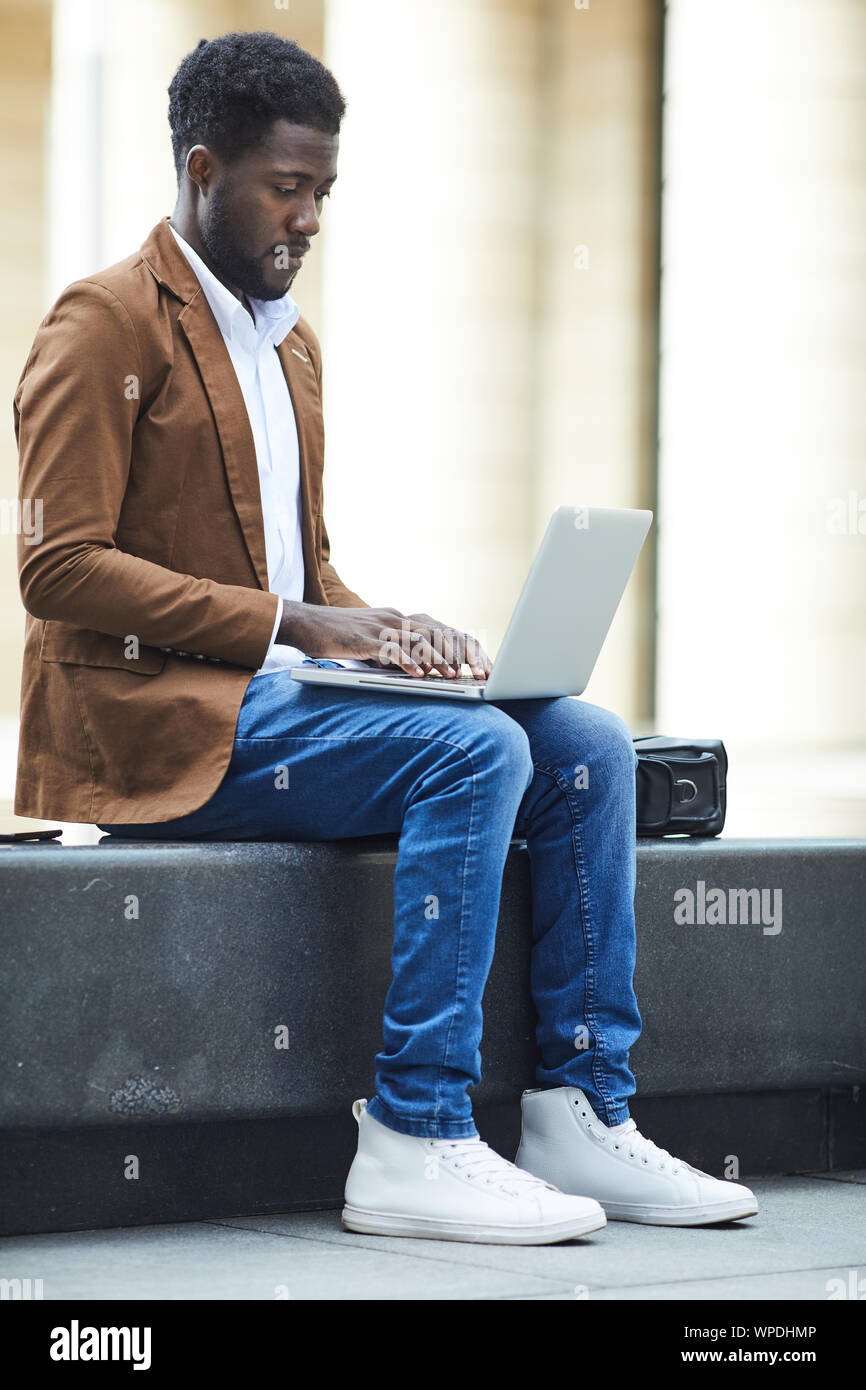 Full length side view of young African-American man using laptop ...