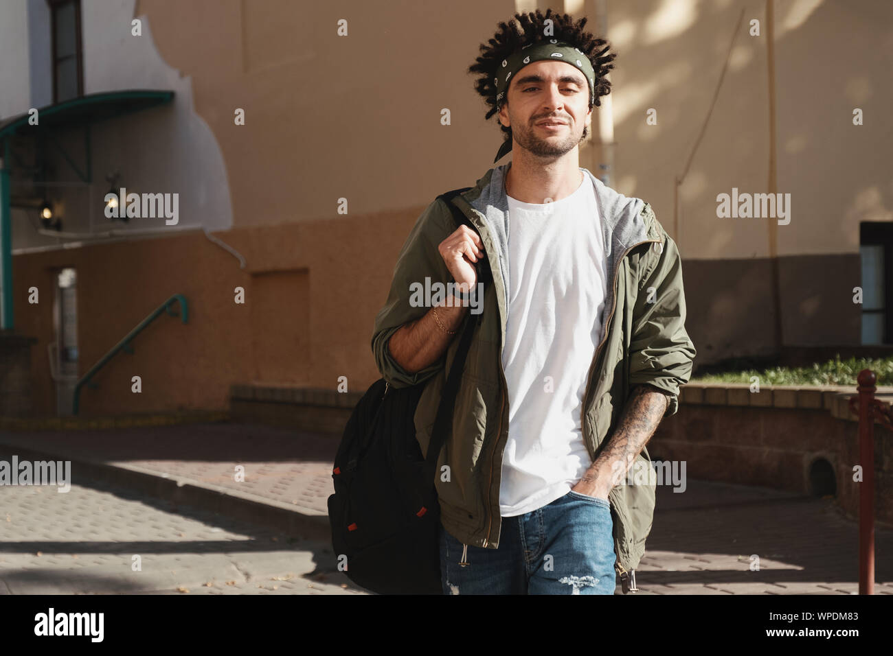 Handsome bearded young man with dreadlocks hairstyle dressed fashionable clothes walking in city street. Autumn fashion outfit, outdoor portrait, urba Stock Photo