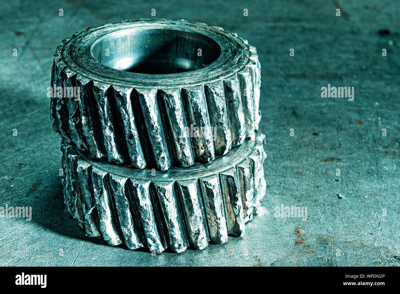 Two very worn out gears on a metal plate in cool petrol tone. Stock Photo