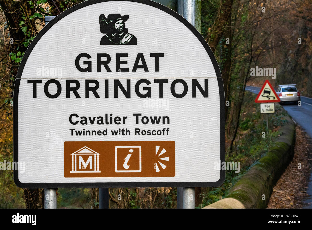 Great Torrington Official Welcome and Information Road Sign on the Main A386 Road into the Town With Warning ‘Bends’ Sign and a Passing Car. Stock Photo
