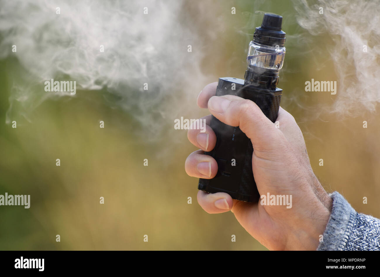 A vaping mod being held in a man's hand with vaping mist surrounding it Stock Photo