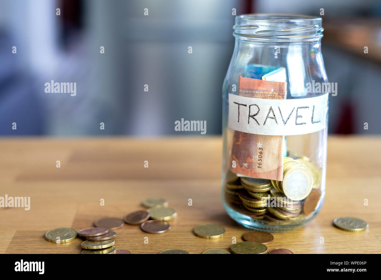 Transparent glass jar labeled travel with euro notes and euro coins inside. Euro coins outside on top of a wooden table. Stock Photo