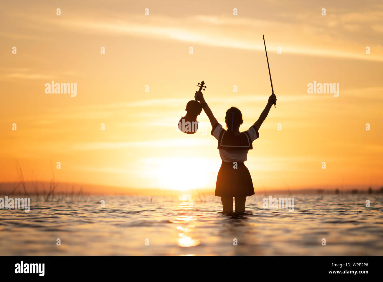 Girl Playing Violin On Water With Sunset Background Stock Photo