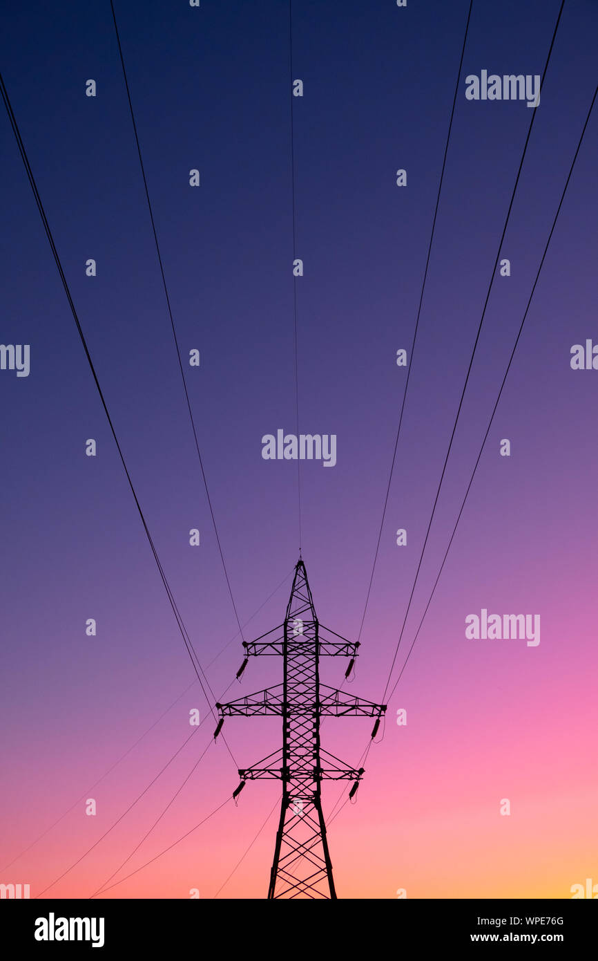 Electric power lines in the evening sun. Electric energy transmission pole in vibrant background, concept of electricity Stock Photo