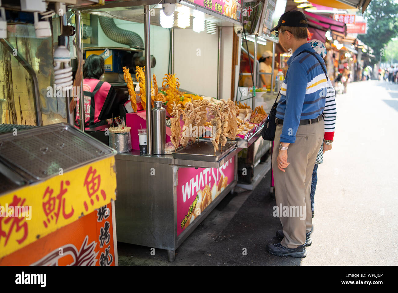 Elderly couple buying traditional crispy deep fried squid at a street food stall on the Danshui (Tamsui) main street at day. Stock Photo