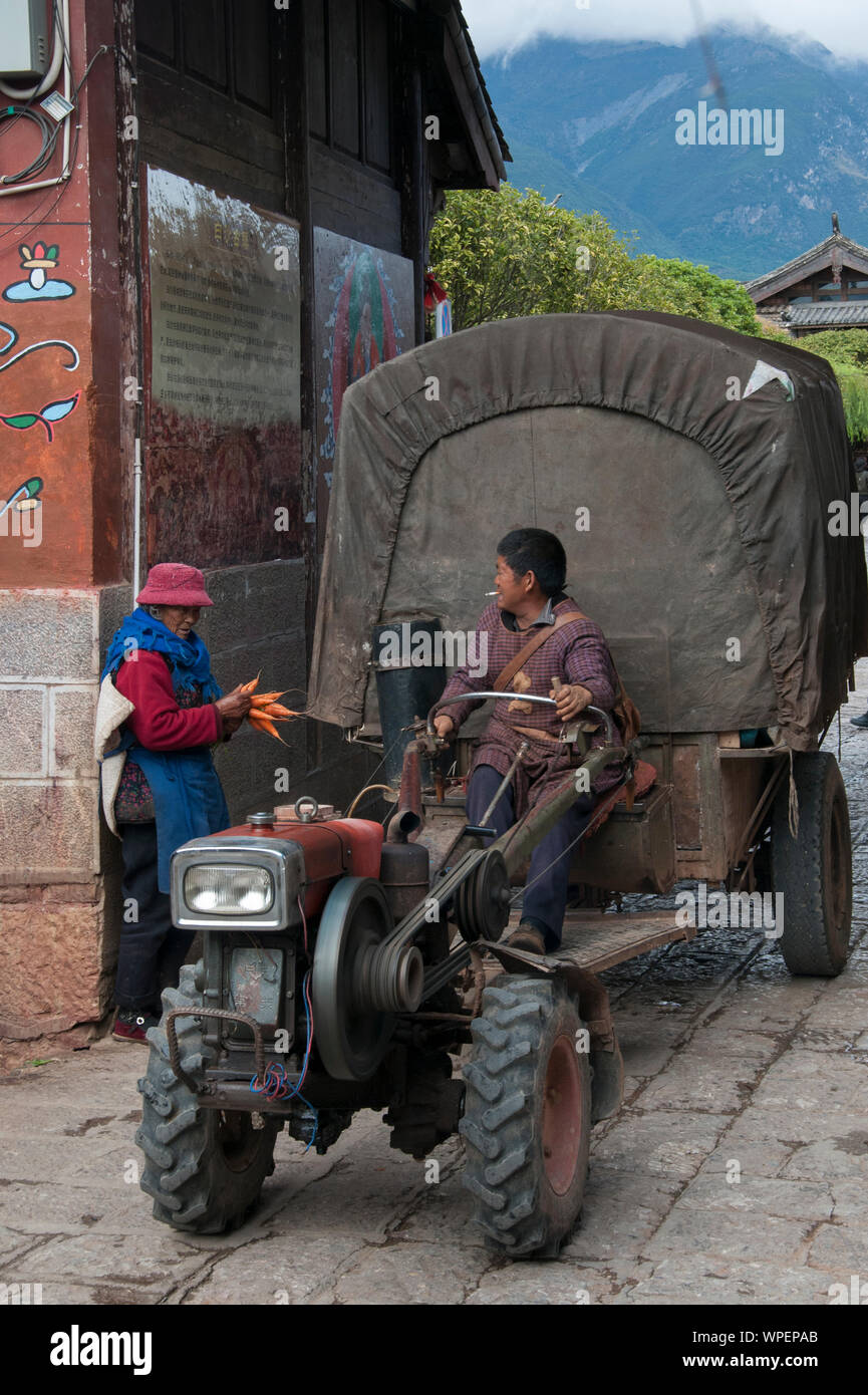 Naxi woman in traditional dress converses with the driver of a farm vehicle at Shuhe, on the Tea Horse Road, outside Lijiang, Yunnan, China Stock Photo