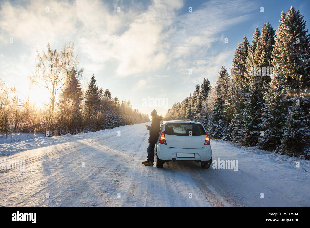 Young man is standing near the car on a winter road. Stock Photo