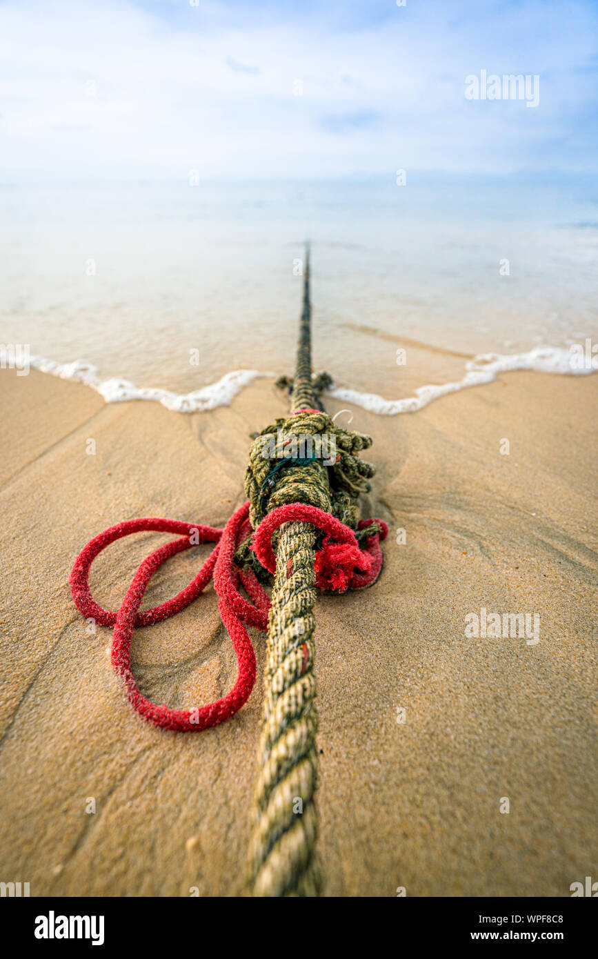 Creative red knotted ships rope lying on a sandy beach leading out to sea on the shoreline as the tide comes in. Stock Photo