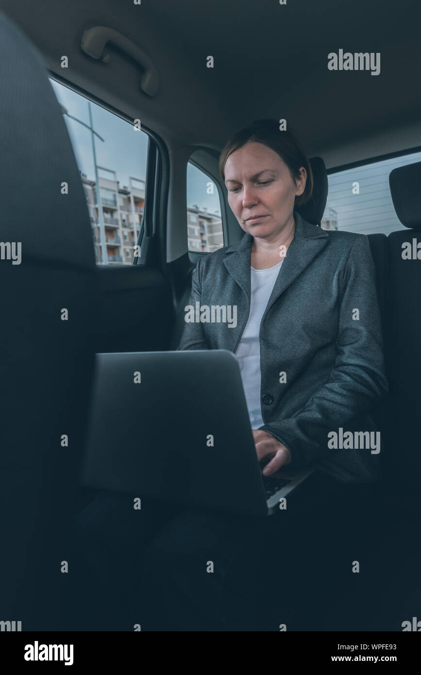 Businesswoman using laptop computer at back seat of company car, business on the move concept with female entrepreneur using modern technology Stock Photo