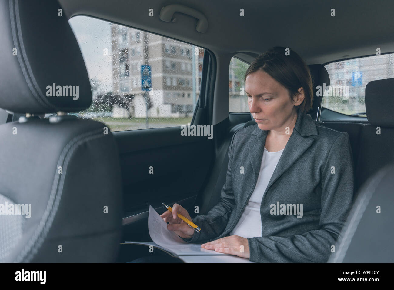 Businesswoman doing business paperwork on car back seat, adult caucasian female businessperson executive analyzing business results while traveling by Stock Photo
