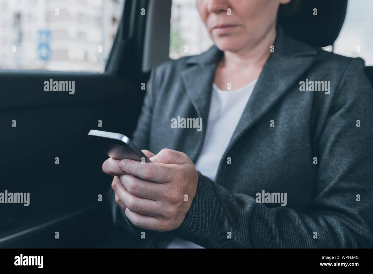 Businesswoman text messaging on mobile phone in car while sitting at the back seat, selective focus Stock Photo