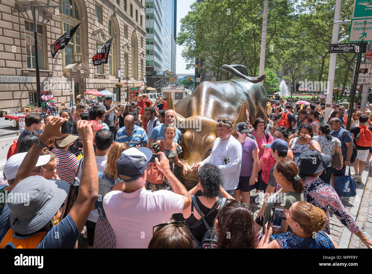New York tourism, view in summer of tourists crowding the Charging Bull sculpture on Broadway in Lower Manhattan, New York City, USA Stock Photo