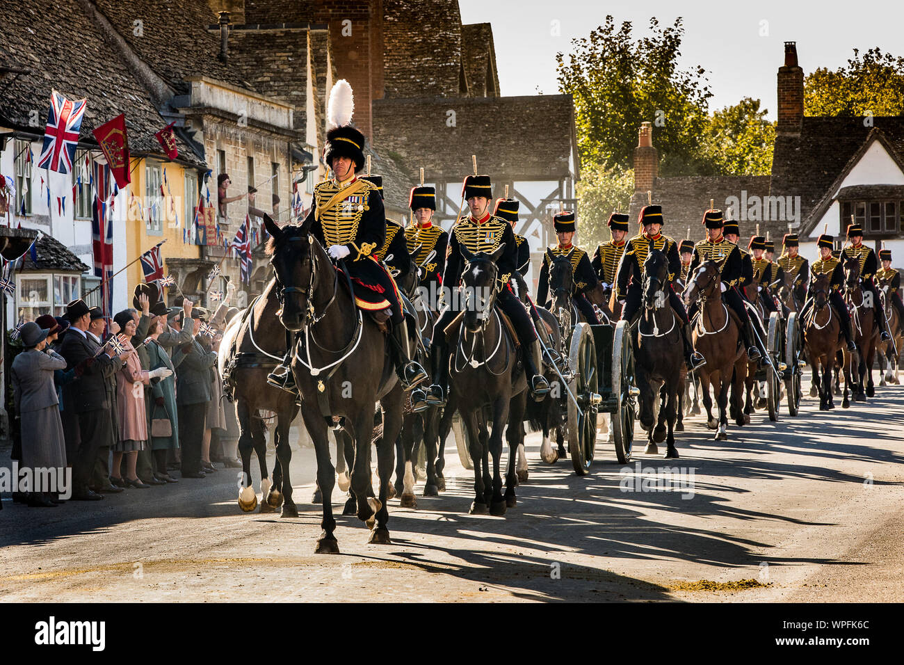 The Kings Troop Royal Horse Artillery during the shooting of a film version of smash TV hit Downton Abbey for cinema. The scene was shot in the High St the National Trust village of Lacock in Wiltshire with 80 horses and Guns and over 250 extras cheering and waving flags as the parade passed by. Stock Photo