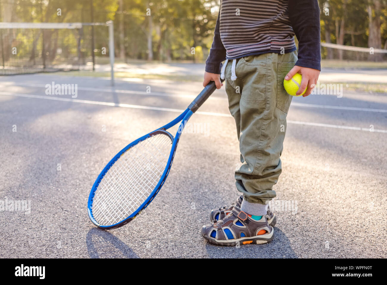 Little australian boy with racket and ball at outdoor tennis court in