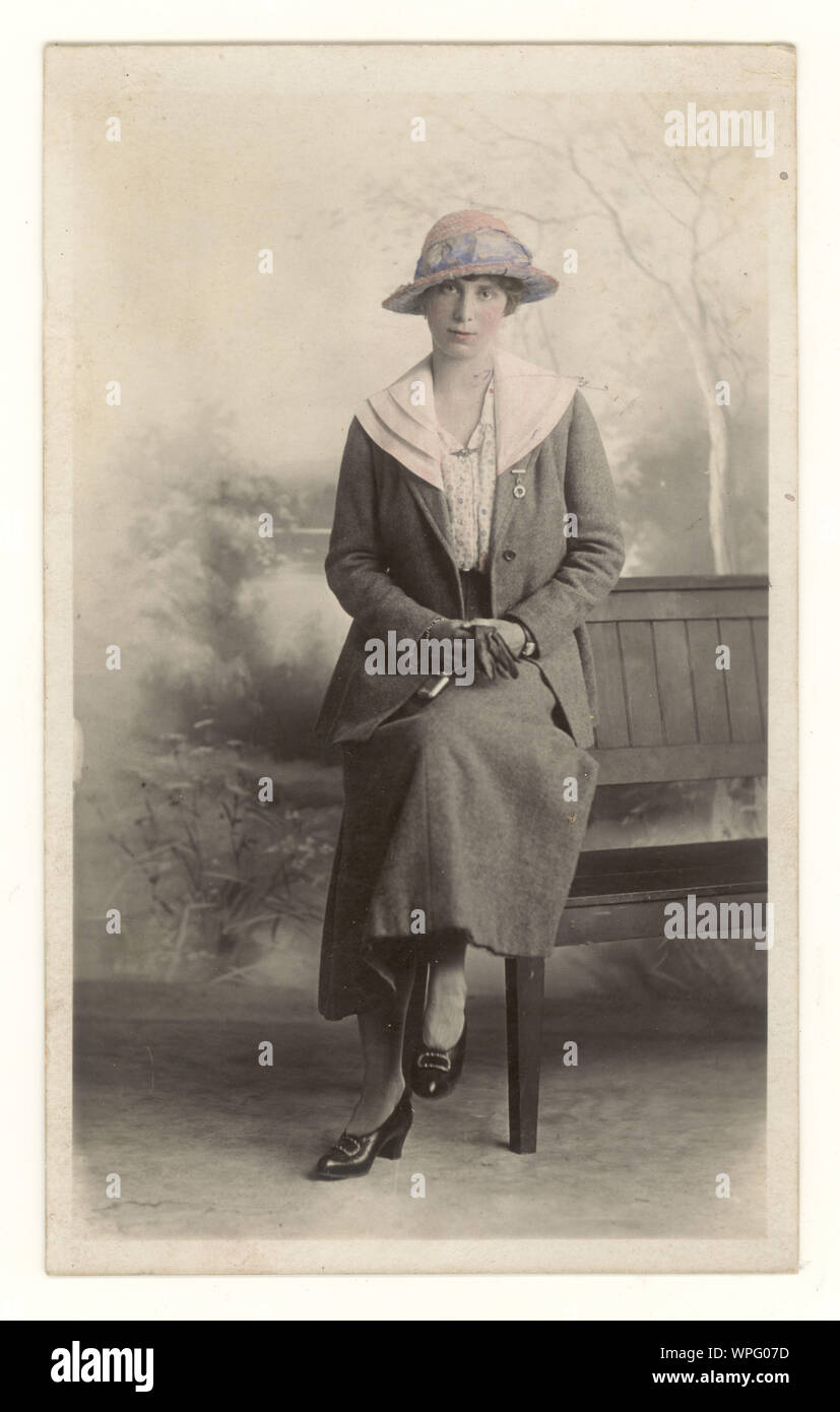 Early 1900's original tinted studio portrait postcard of a pretty young woman wearing a typical skirt and jacket of the period, a hat and with possibly a Royal Flying Corps (RFC) sweetheart brooch on her collar, holding gloves and large locket, Gravesend, Kent, U.K. circa 1915 Stock Photo