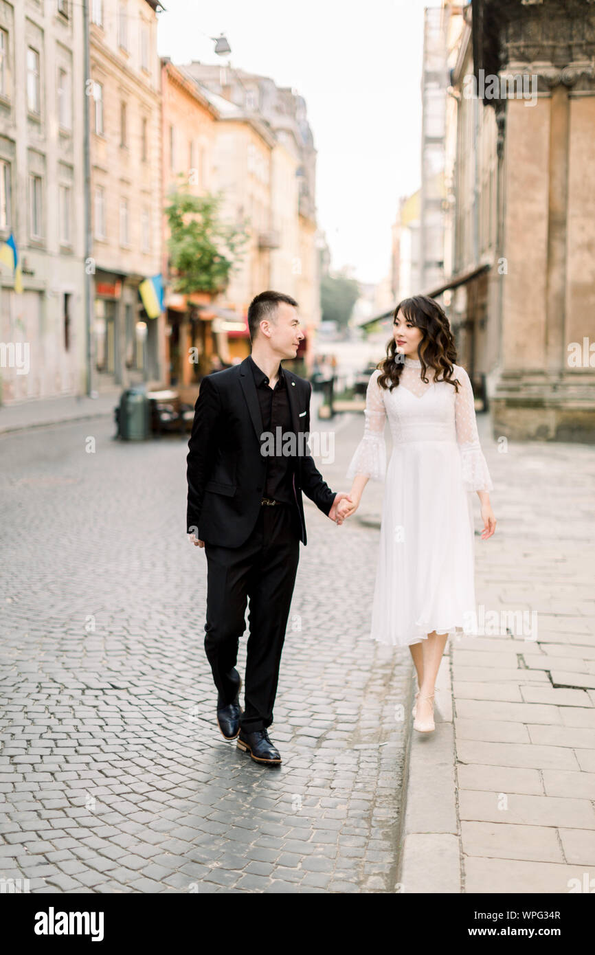 Tender Asian couple in love - bride in white dress and groom in a black suit  on their wedding walk in the old city center. Historical ancient building  Stock Photo - Alamy