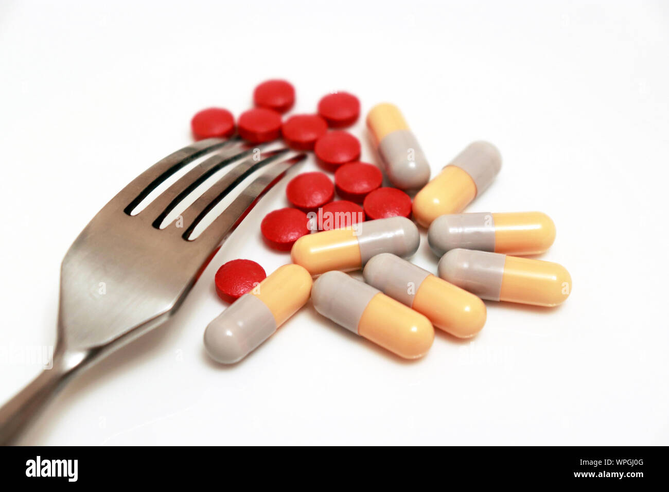 Pills and capsules with fork on white plate. Concept of slimming, diet pills, healthy eating, vitamins, fortified food Stock Photo