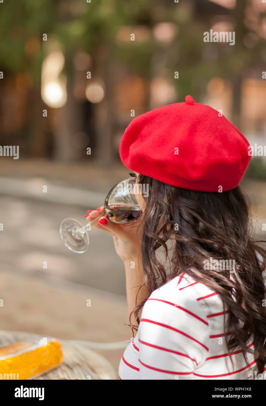 Woman in a red cap and striped t-shirt drinking red wine in outdoor ...
