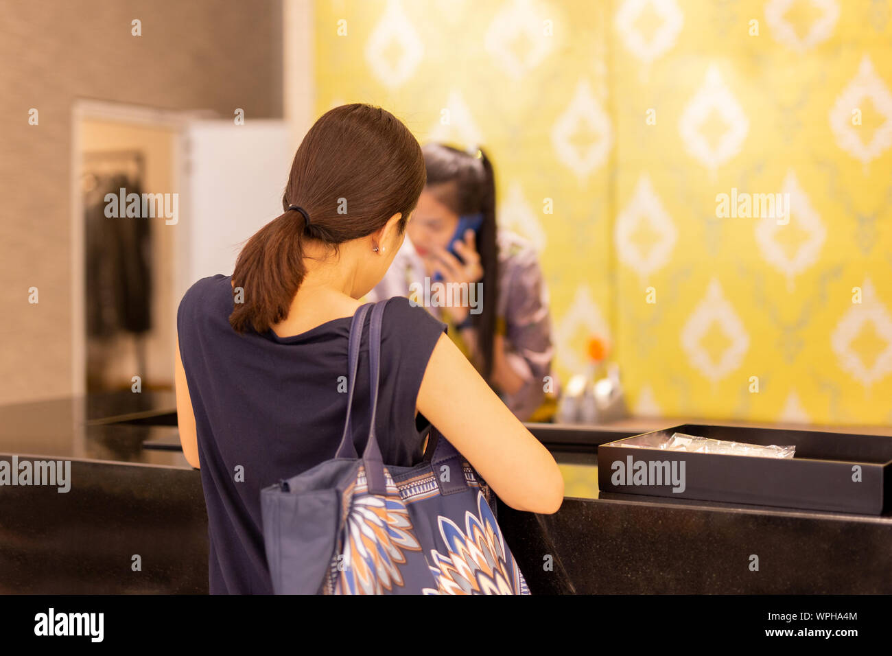 Woman at checkout in clothing store with staff on the phone enquiry. Stock Photo