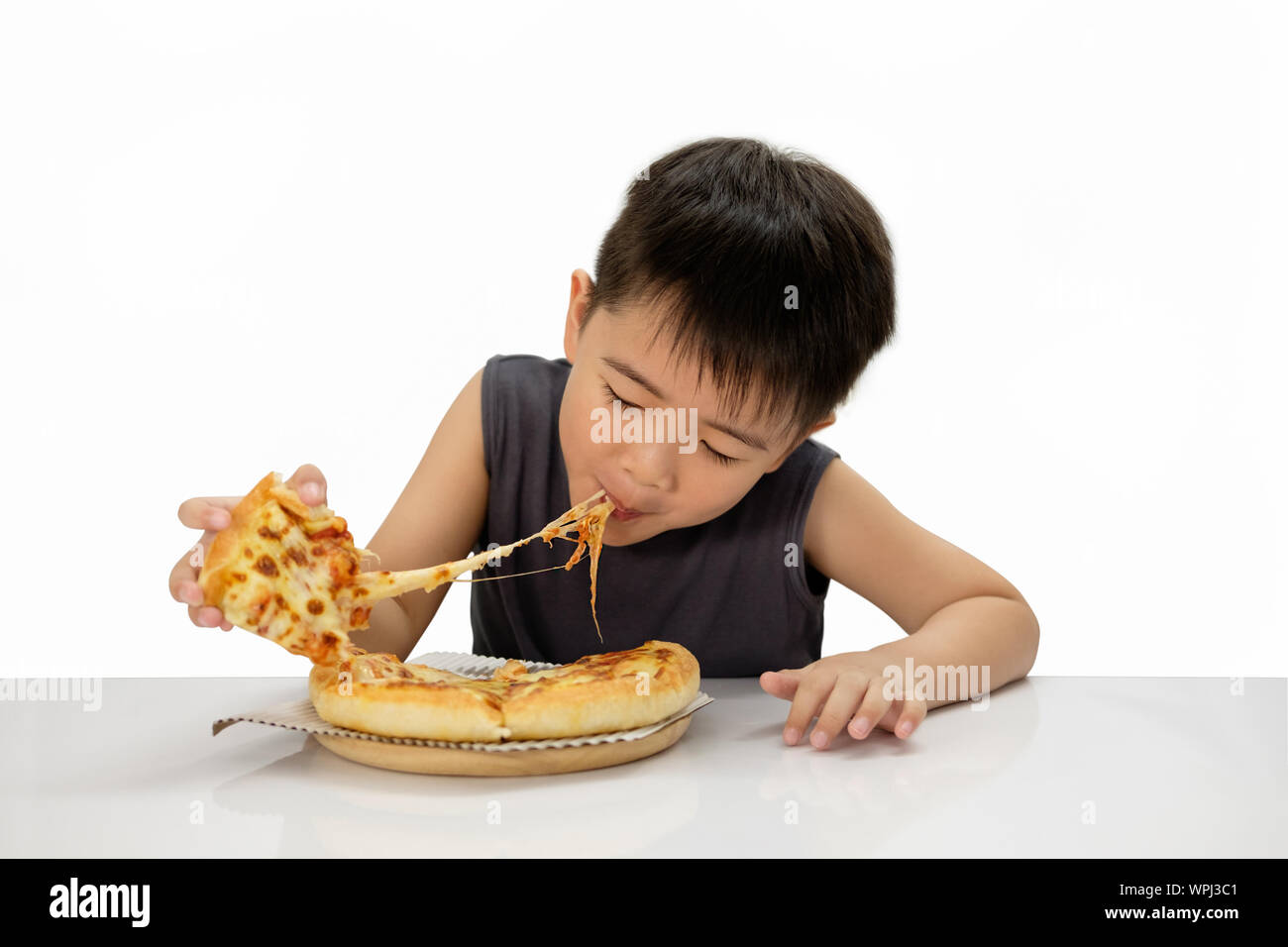 Asian boy  happy to eat pizza with a hot cheese is melting and stretching on a wooden pad.  Isolated on white background, choose fucus point. Stock Photo