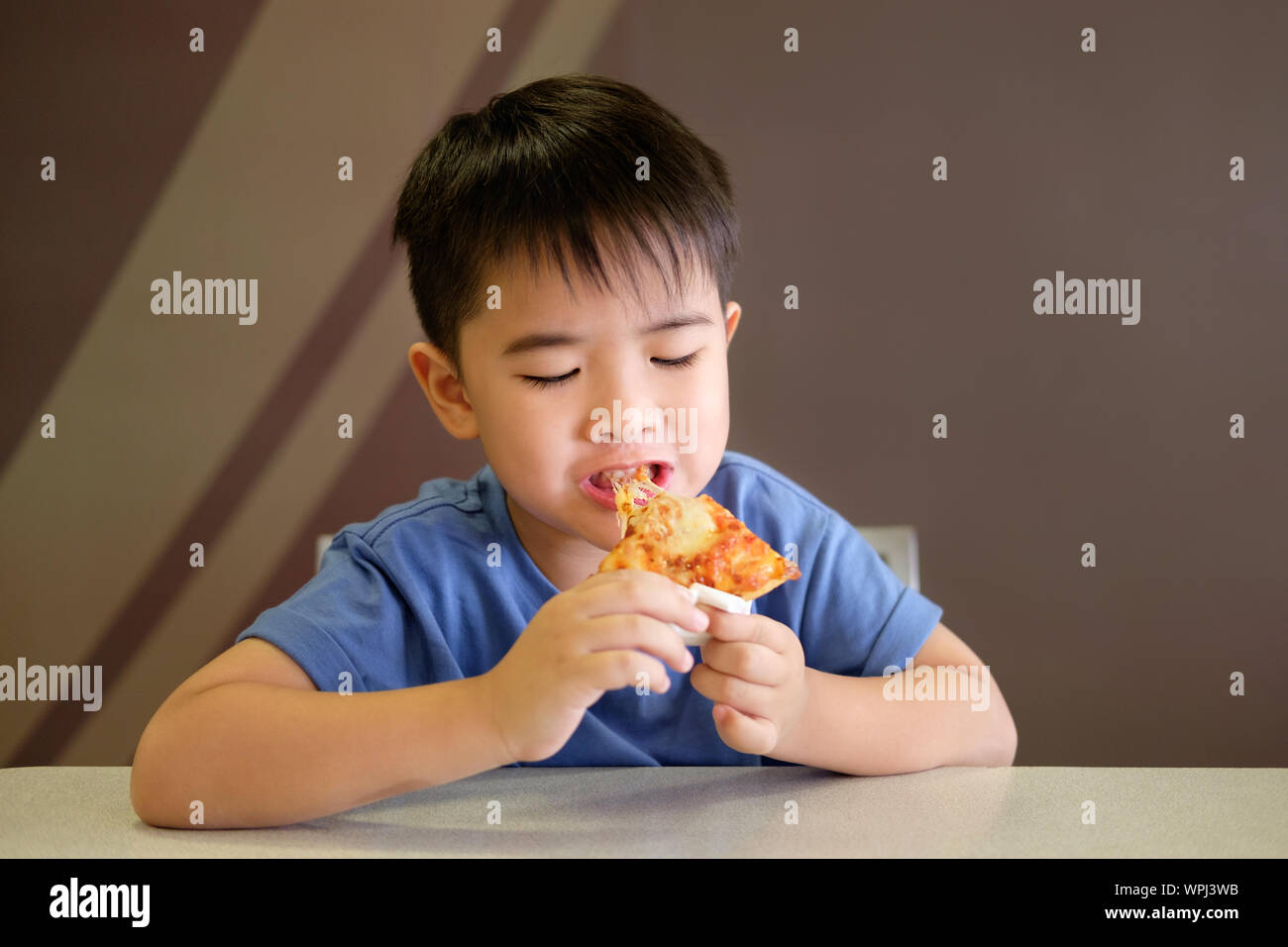 Asian boy is happy to eat pizza on brown background. Stock Photo