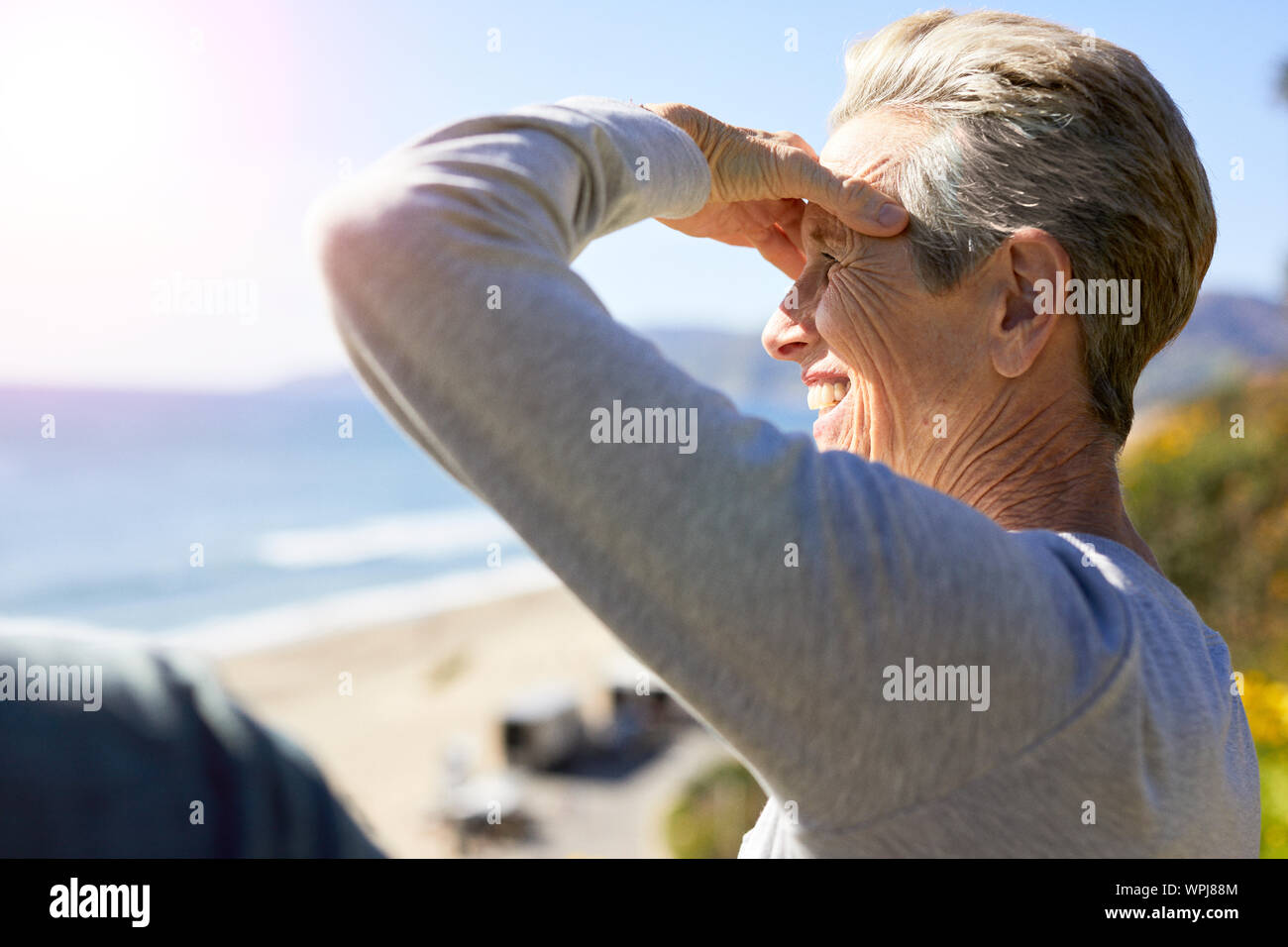 Side view of smiling senior woman shielding eyes against beach Stock Photo