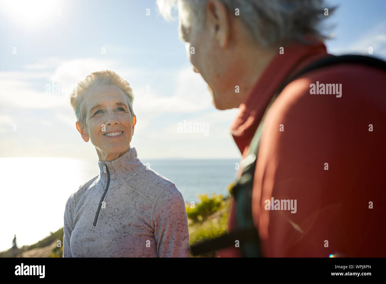 Smiling senior woman looking at man while standing against sky during sunny day Stock Photo