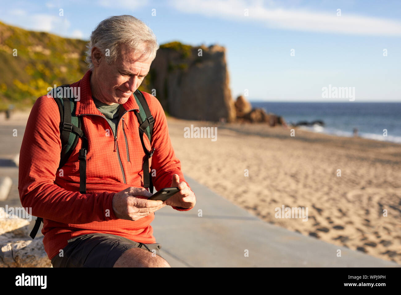 Senior man using smart phone while standing at beach Stock Photo
