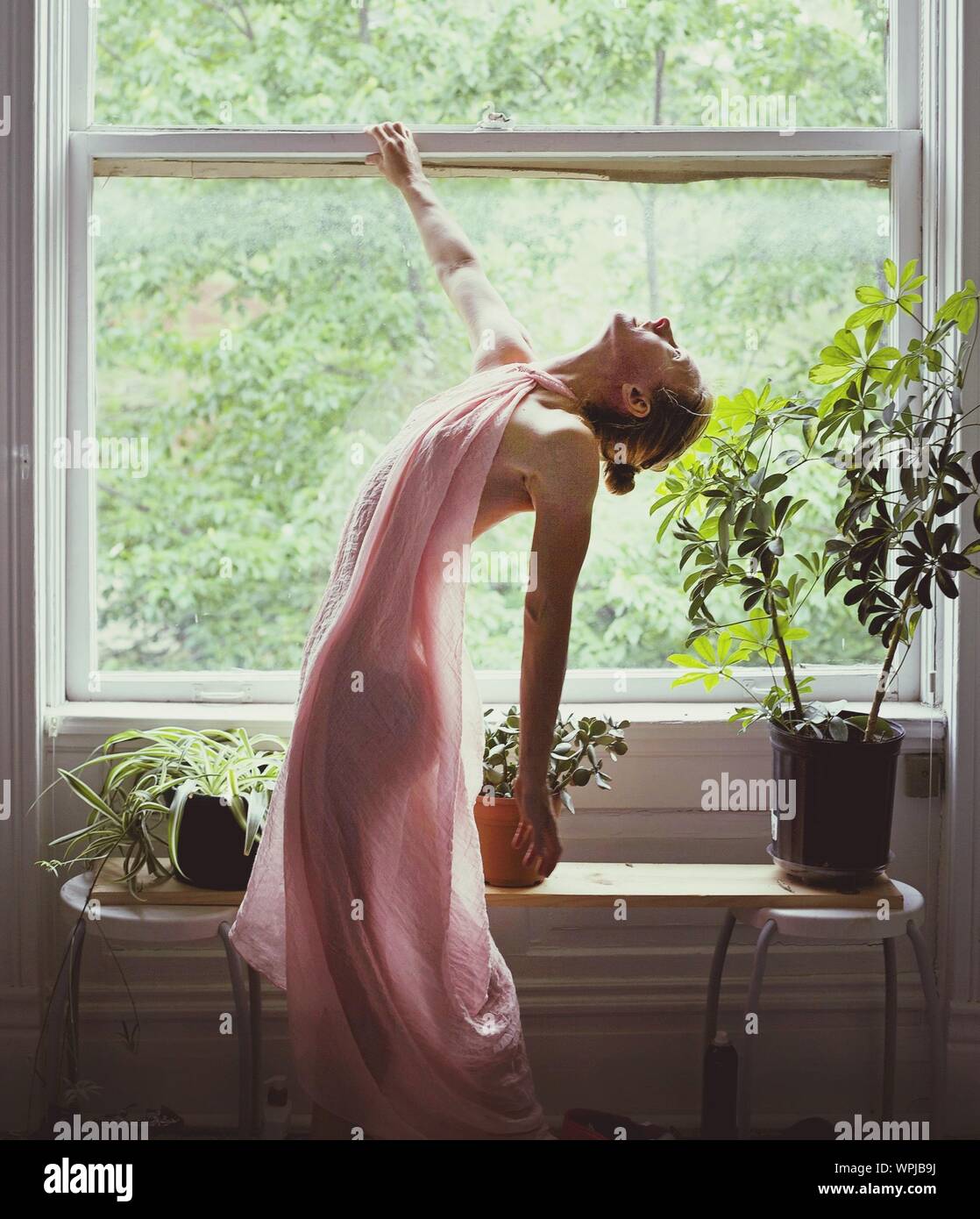 Side View Of Beautiful Woman Bending Backward By Window Stock Photo