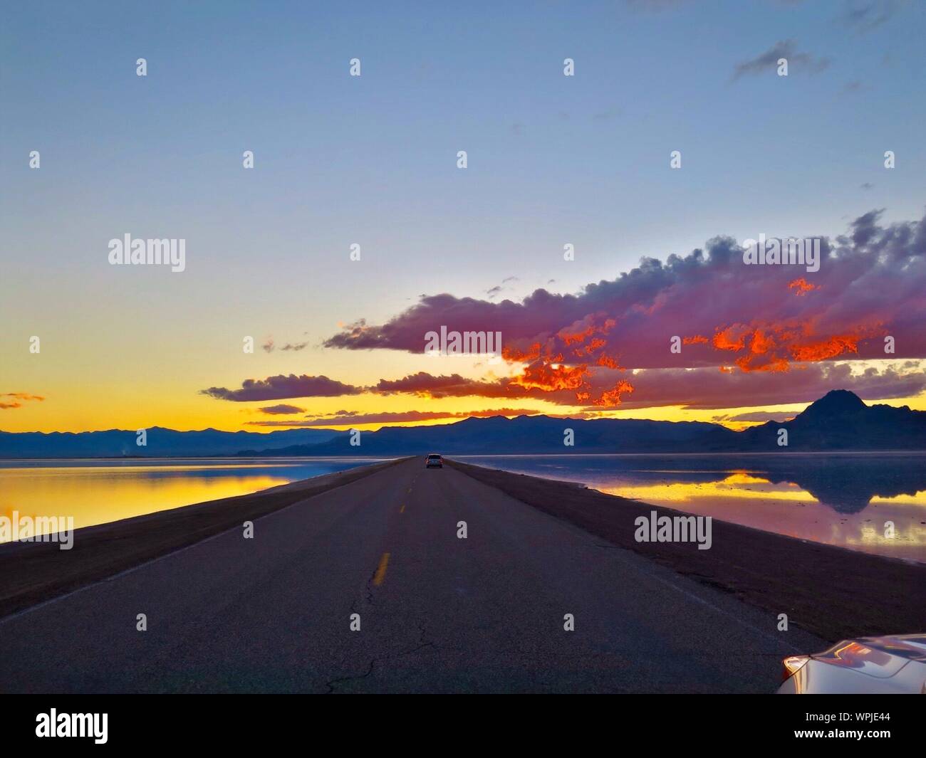 Empty Road Amidst Salt Flats Against Cloudy Sky During Sunset Stock Photo