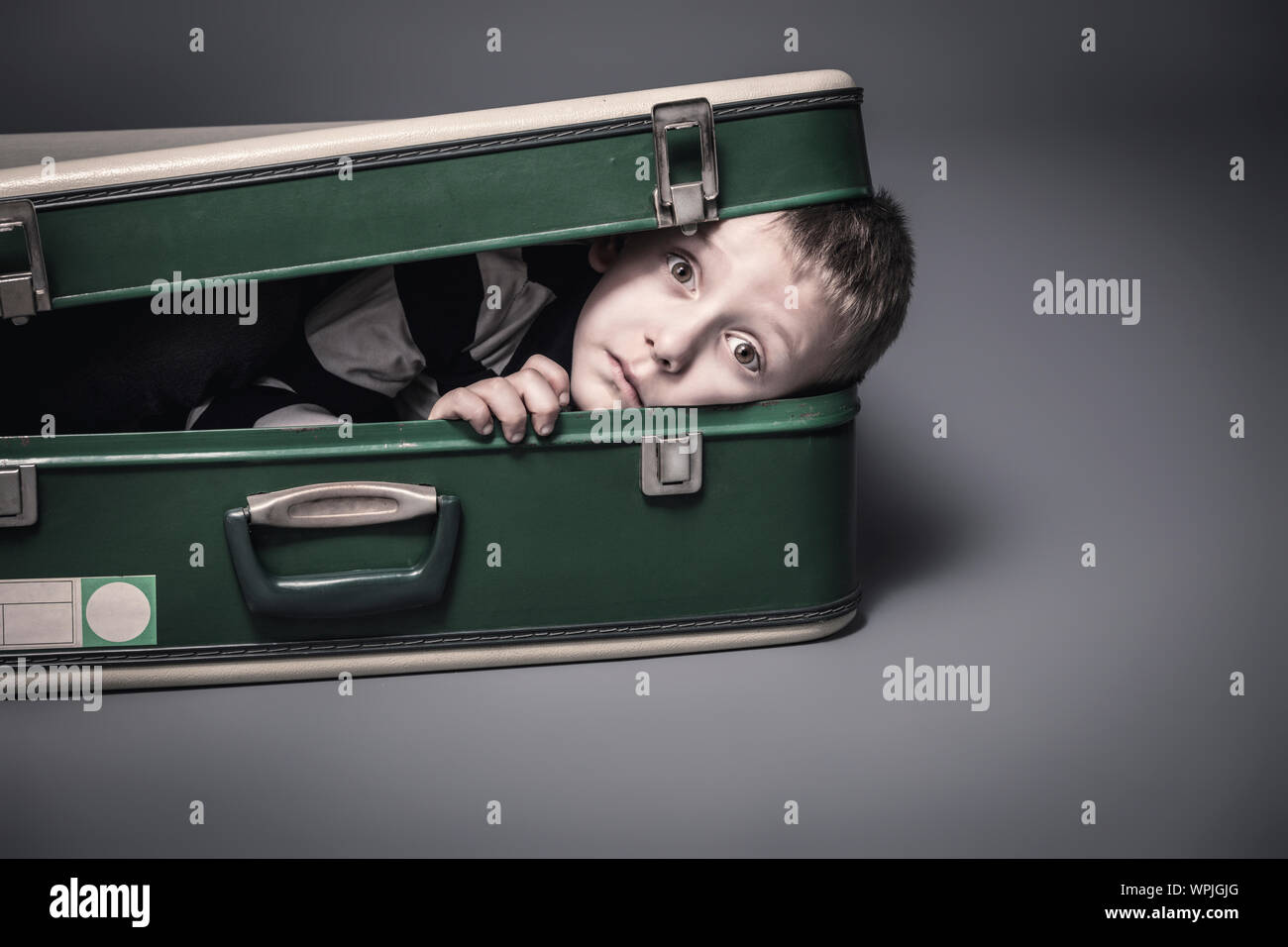 6 year old caucasian boy hides in an old suitcase, studio portrait. Stock Photo