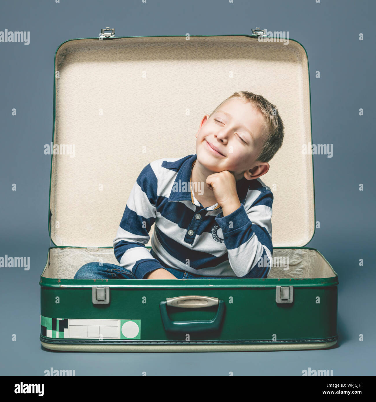 child sitting in an old suitcase smiles imagining a journey or an adventure. Stock Photo
