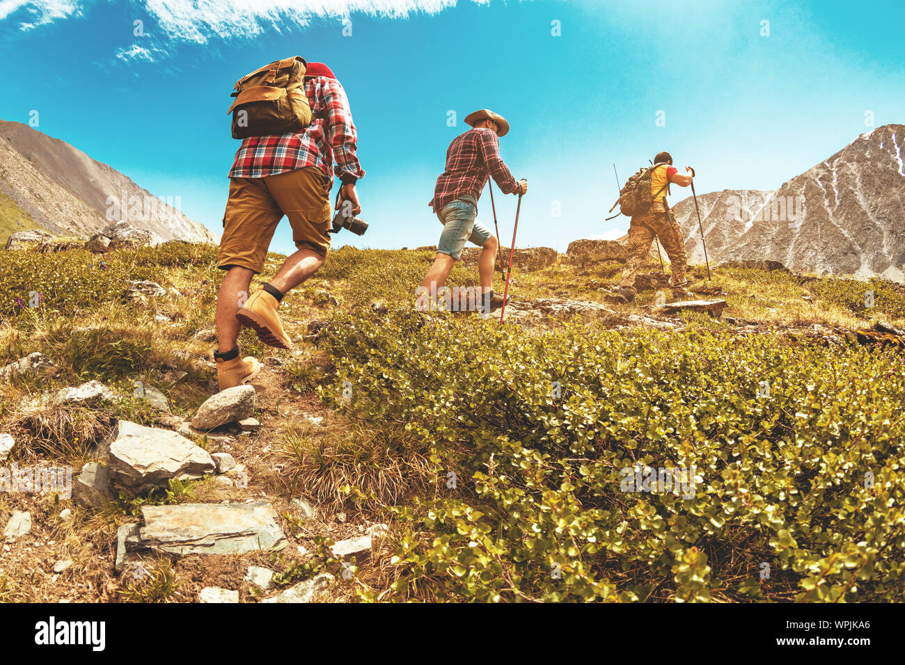 Group of three tourists hikers or friends trekking uphill in mountains Stock Photo